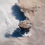 volcanic ash cloud rising above an island