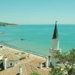 A dry Mediterranean coastline with parched land above a blue sea.