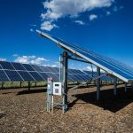 Rows of solar panels stretching across desert land under a clear sky.