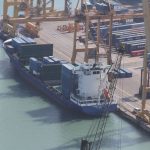 A container ship being loaded by cranes at a busy port